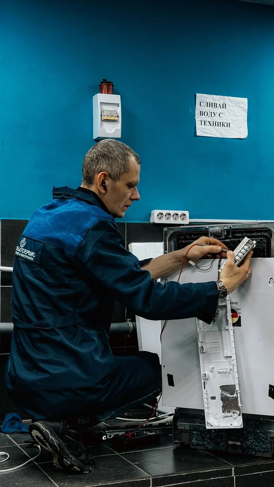 Technician in a work jacket testing wiring on an appliance control with a meter probe