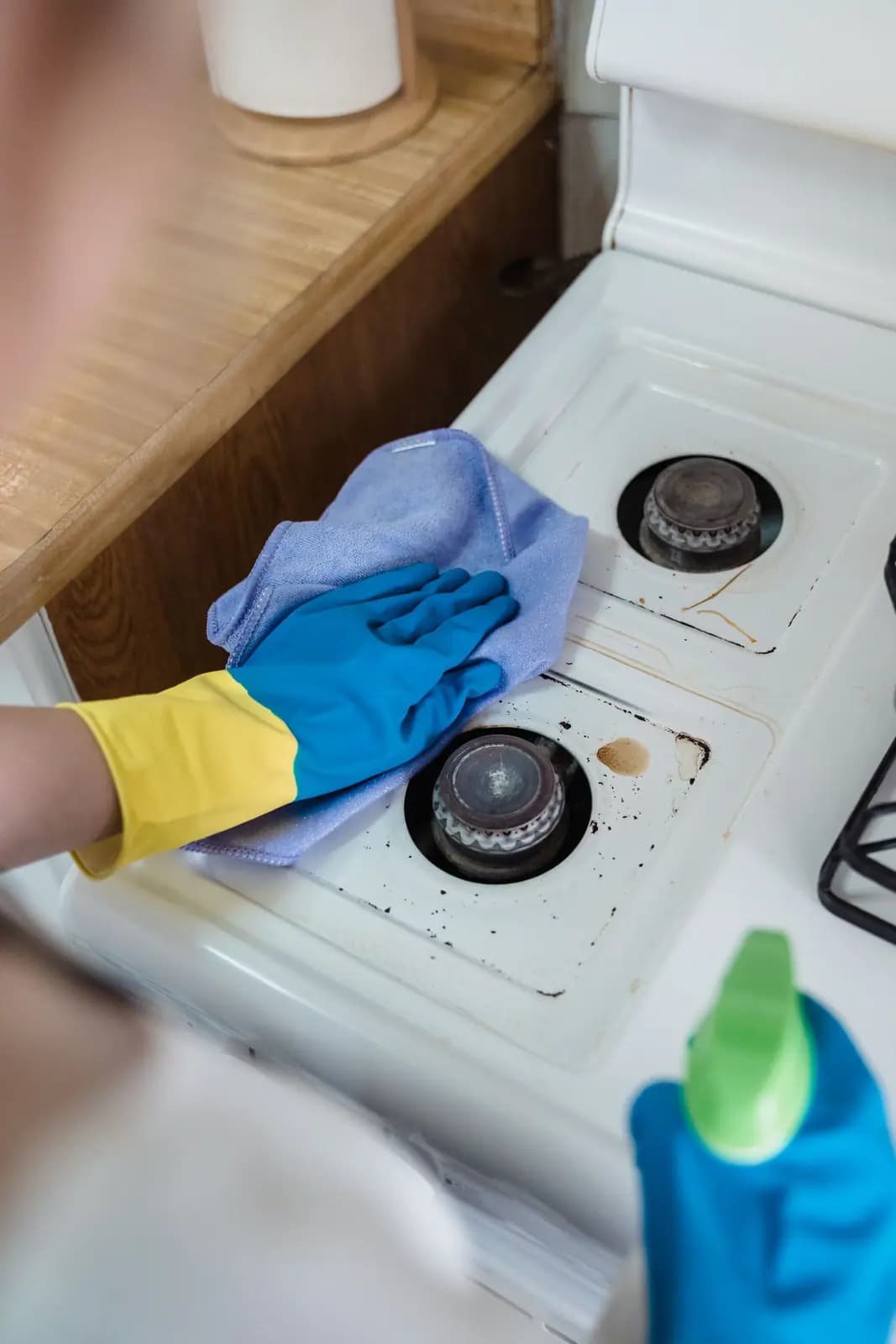 Gloved hand wiping a white gas cooktop with spill stains and burnt spots around two burners