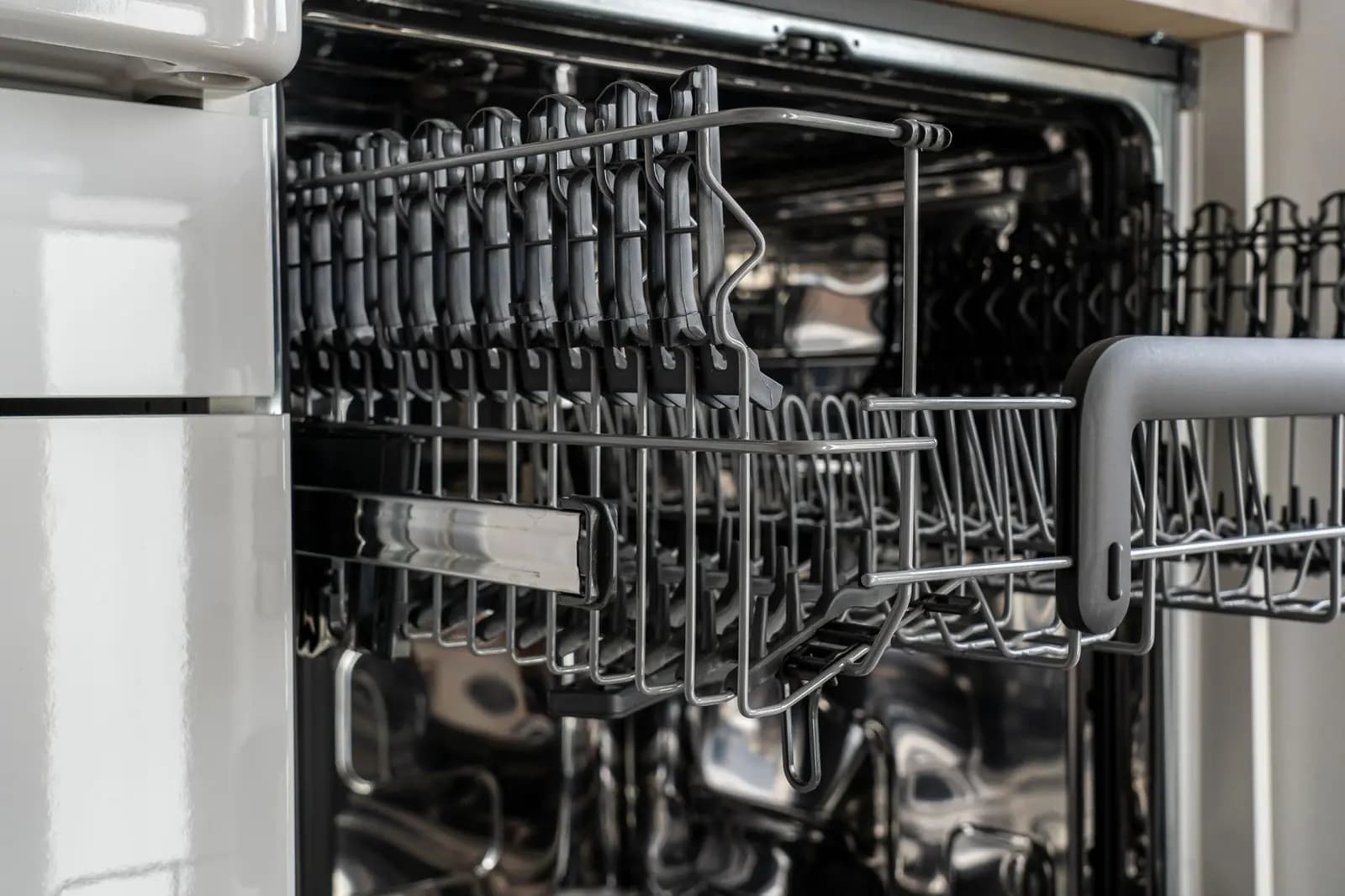 Empty dishwasher lower rack and spray arm inside a stainless tub