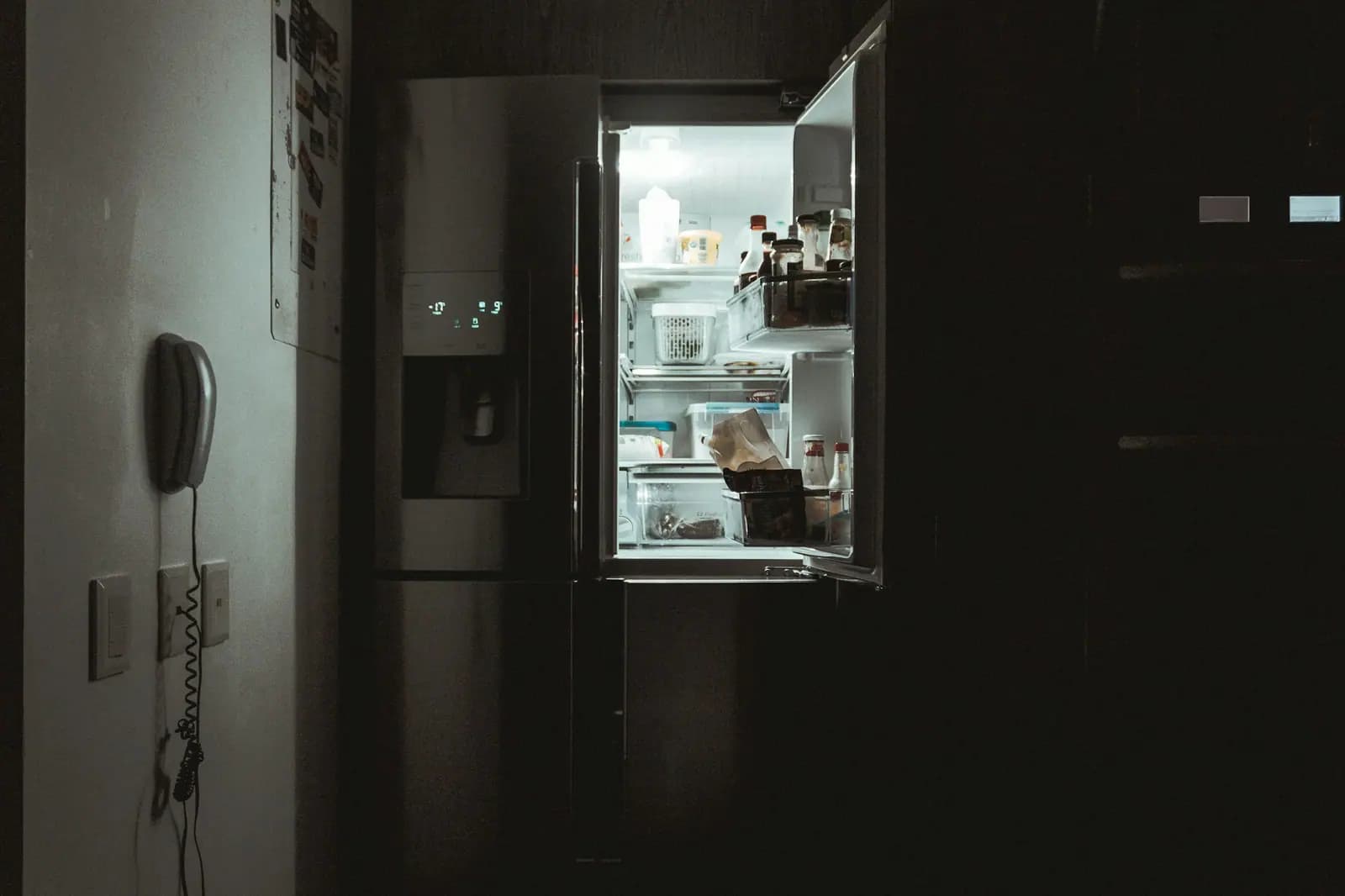 Refrigerator door open in a dark kitchen with the interior light on